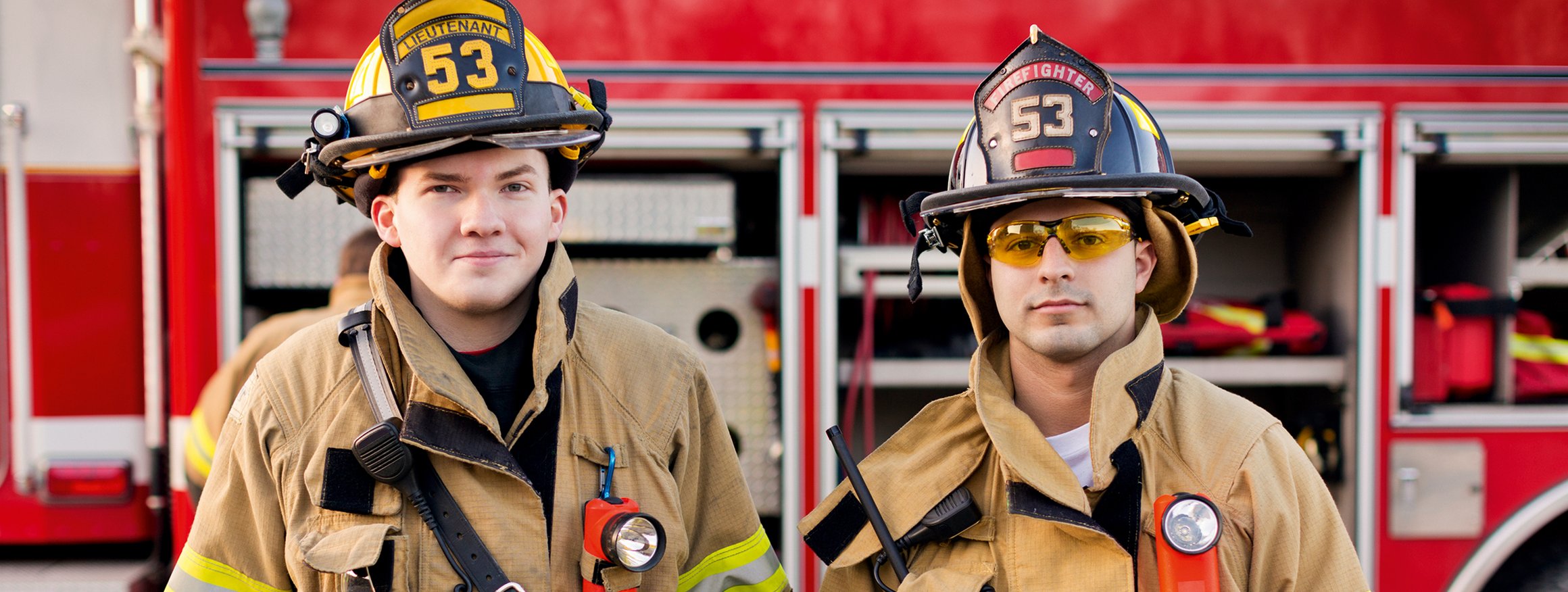 Zwei Feuerwehrmänner stehen in Arbeitskleidung vor einem Einsatzwagen