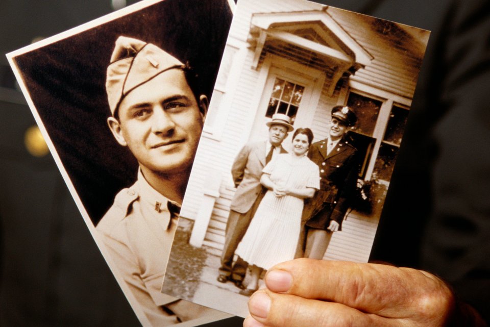 Ein alter Mann in Uniform hält in der Hand zwei alte Fotografien und erinnert sich an den 2. Weltkrieg