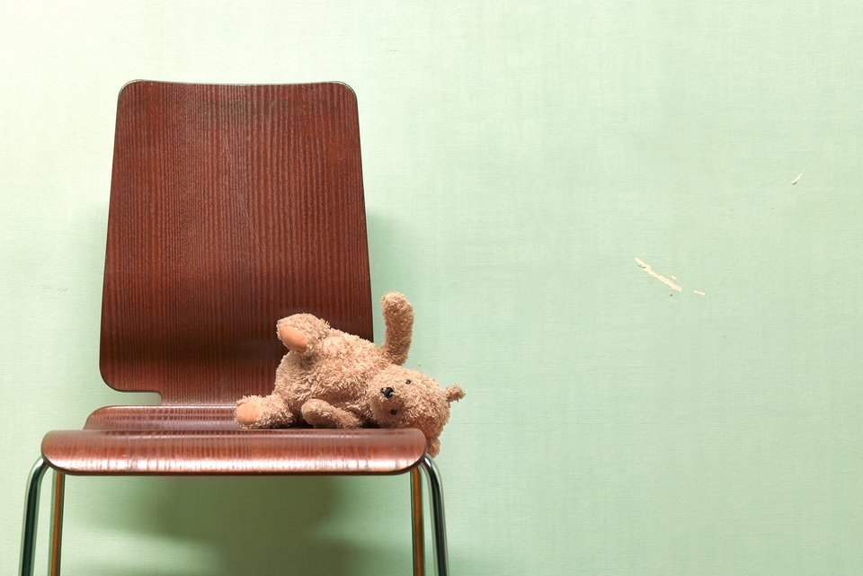 Ein Teddybär liegt auf einem Holzstuhl, der vor einer grünen Wand steht.