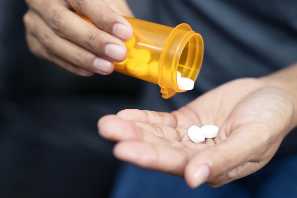 Eine Hand hält eine gelbe Tablettendose und lässt zwei weiße Tabletten in die andere Hand hineinfallen