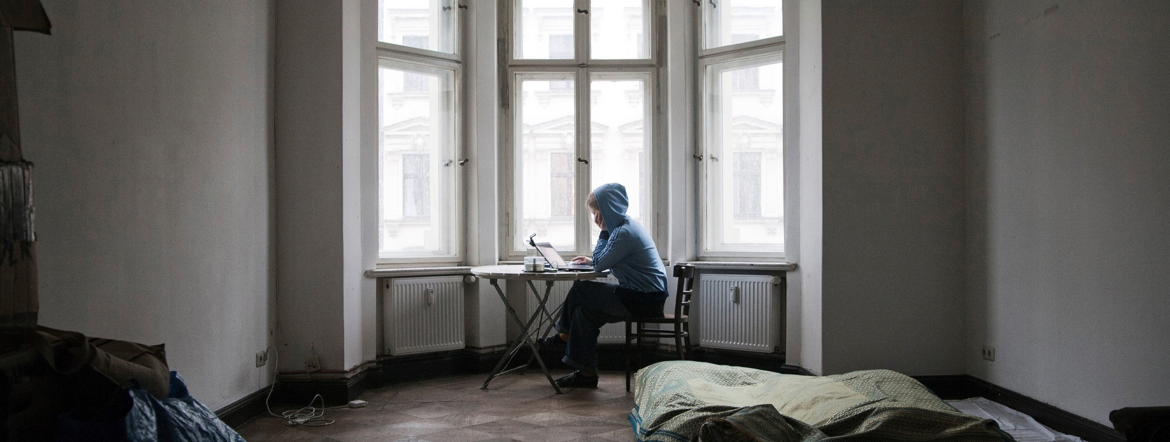 Eine Frau sitzt einsam in einer Stadtwohnung an ihrem Laptop am Fenster in einem Erker