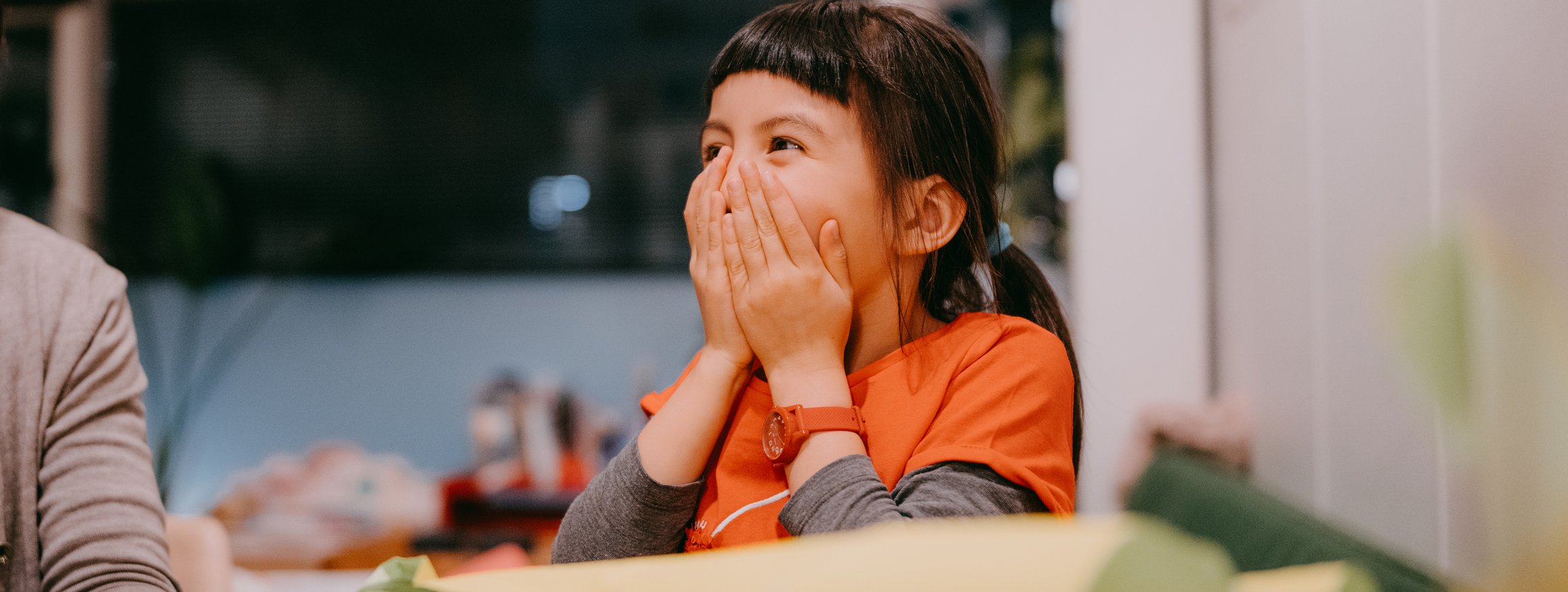 Ein Kind wird auf seiner Geburtstagsfeier überrascht und hält lachend die Hände vor Nase und Mund