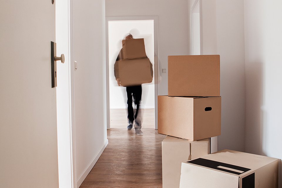 Eine Person zieht um und trägt Umzugskartons in eine leere Wohnung