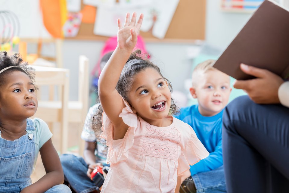 Grundschulkinder sitzen auf dem Boden mit ihrem Lehrer und haben Freude am Lernen