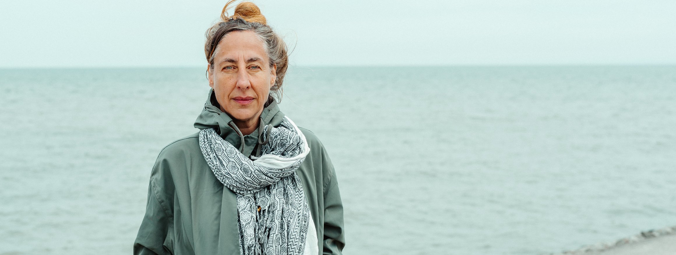 Die Schriftstellerin Judith Herrmann steht mit Mantel und Schal an einem Strand, hinter ihr das graue Meer