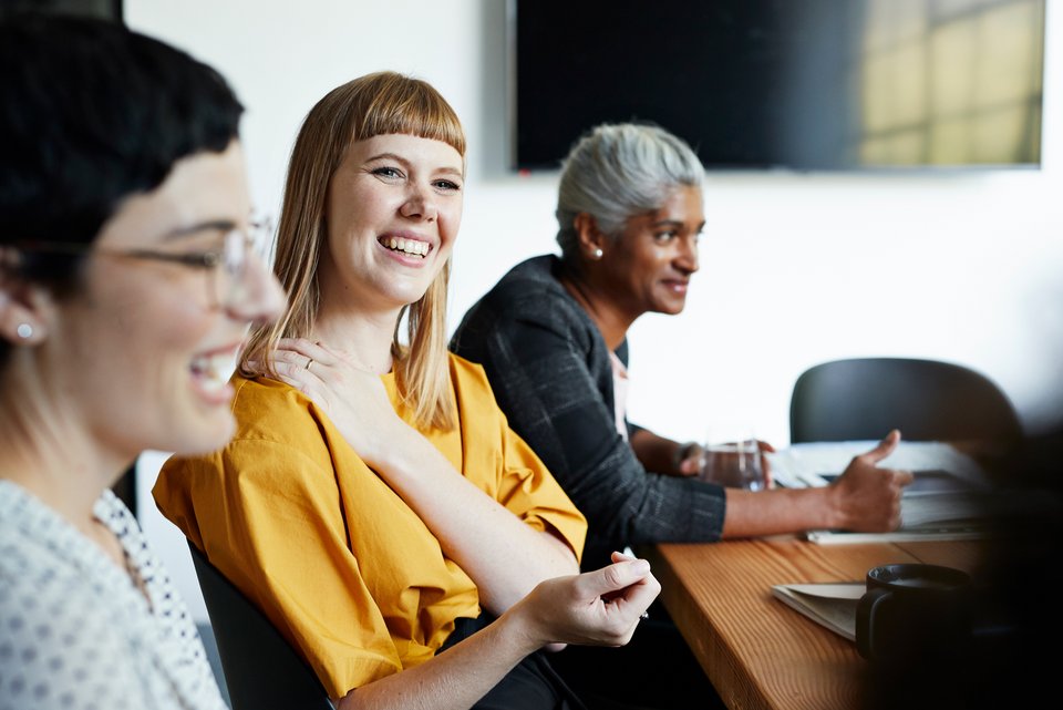 Ein Team sitzt lachend in einem Meeting und kooperiert miteinander 