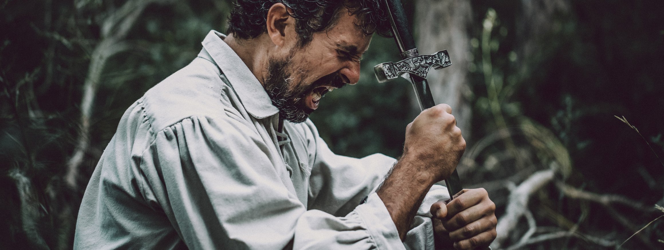 Ein Schauspieler mit einem altertümlichen Hemd umfasst verzweifelt ein Schwert, wobei er seinen Emotionen freien Lauf lässt und in seiner Rolle aufgeht