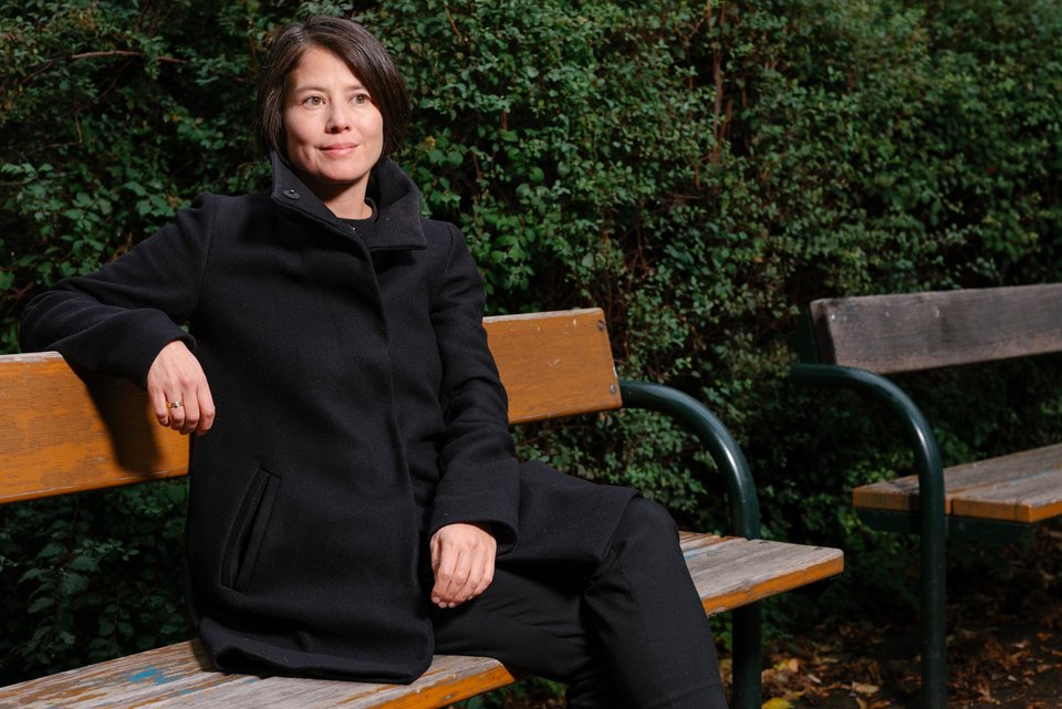 Die Autorin Milena Michiko sitzt auf einer Parkbank vor einer grünen Hecke.