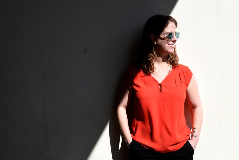 Kate Sweeny, ein Shootingstar in der psychologischen Forschung, trägt Sonnenbrille und steht mit Händen in den Taschen, entspannt lächelnd in der Sonne