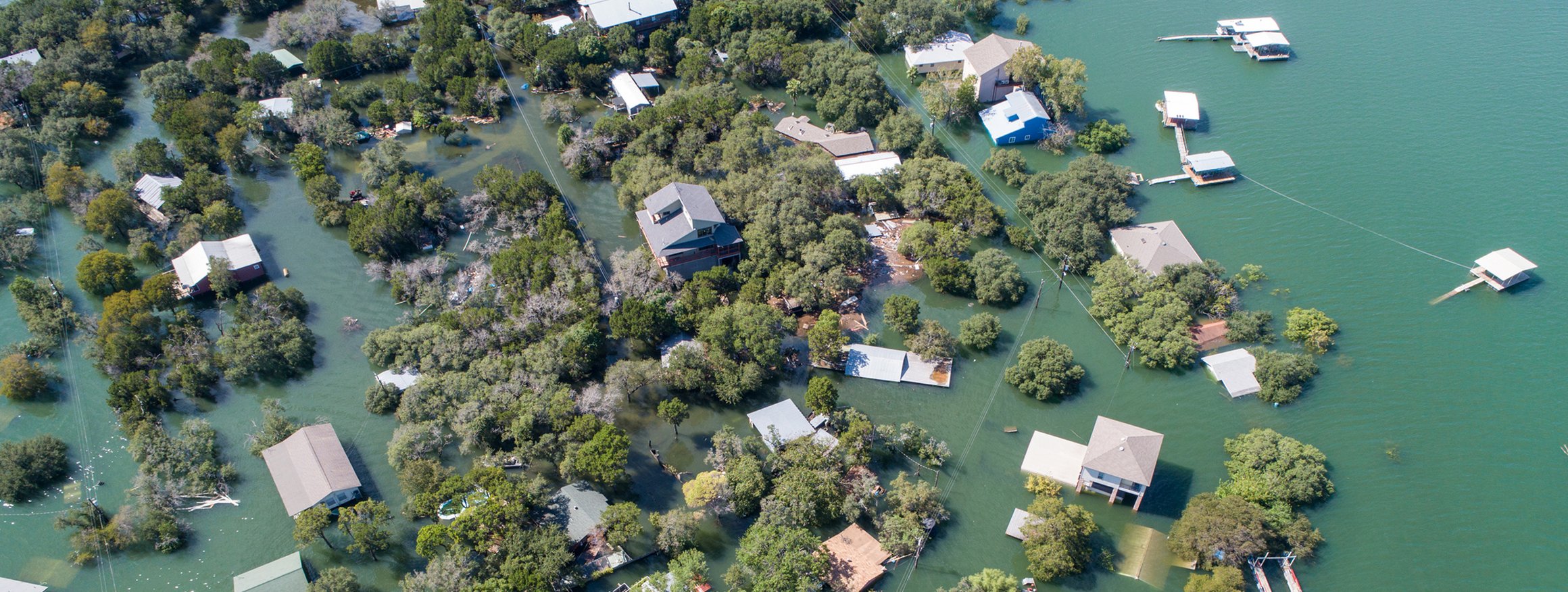 Eine Landschaft wurde von einem Fluss überflutet und man sieht von den Häusern größtenteils nur die Dächer aus dem Wasser ragen