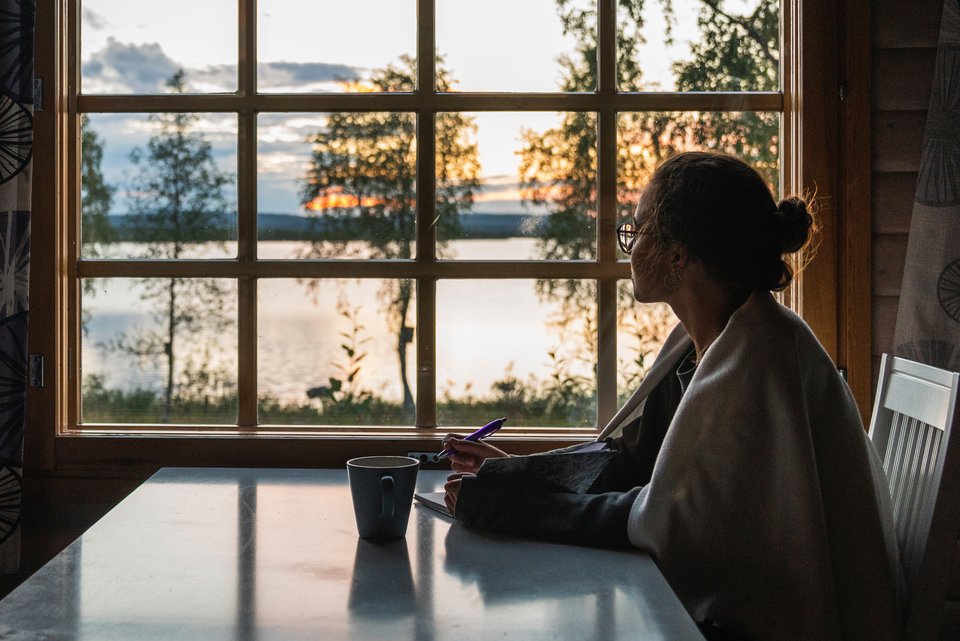 Das Foto zeigt eine Frau, die am Tisch sitzt und in ein Notizbuch schreibt