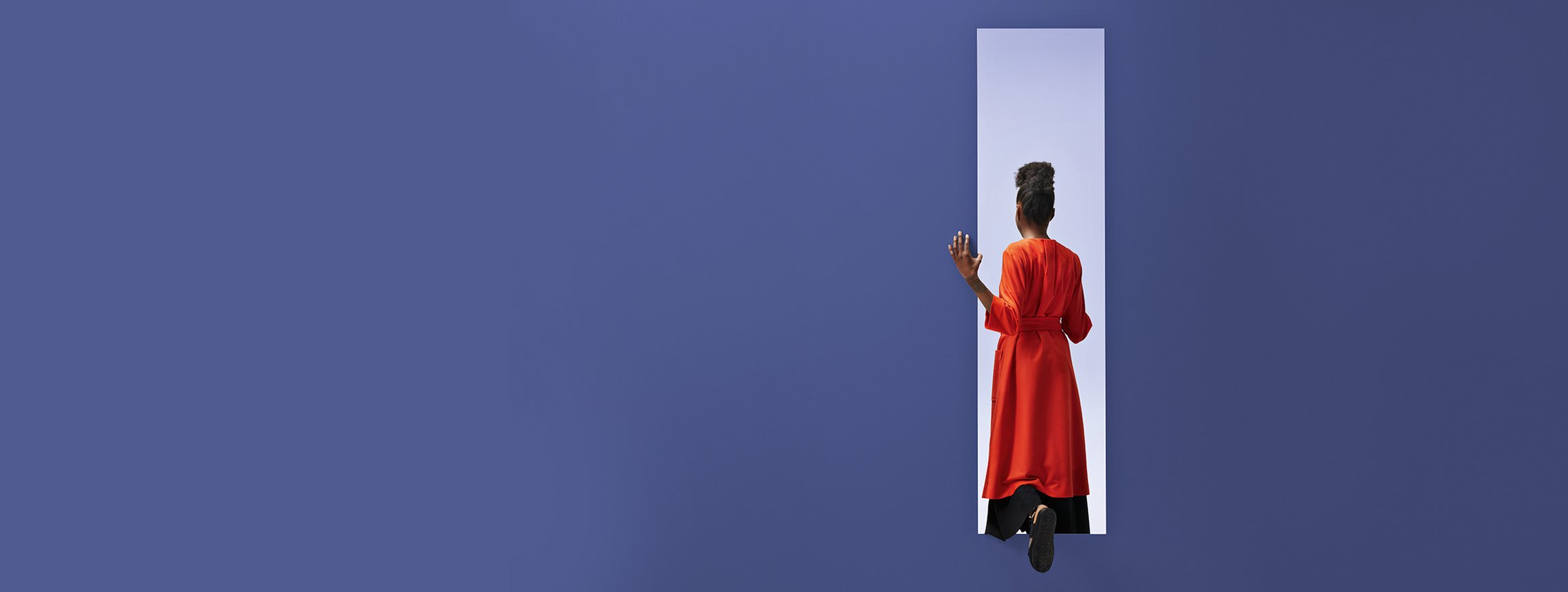 Frau in rotem Kleid geht durch einen Ausgang an einer großen blauen Wand