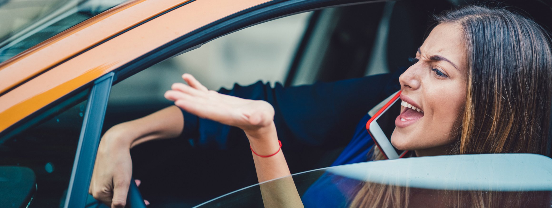 Eine Frau sitzt wütend am Steuer ihres Autos und gestikuliert verärgert aus dem Fenster