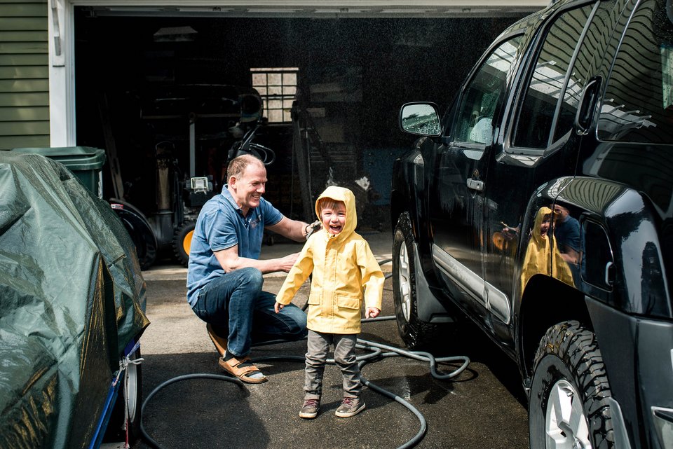 Ein Mann wäscht fröhlich gemeinsam mit einem kleinen Jungen seinen schwarzen SUV