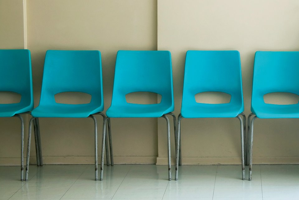 Blaue Plastikstühle stehen im Warteraum eines Arztes vor einer tristen grauen Wand