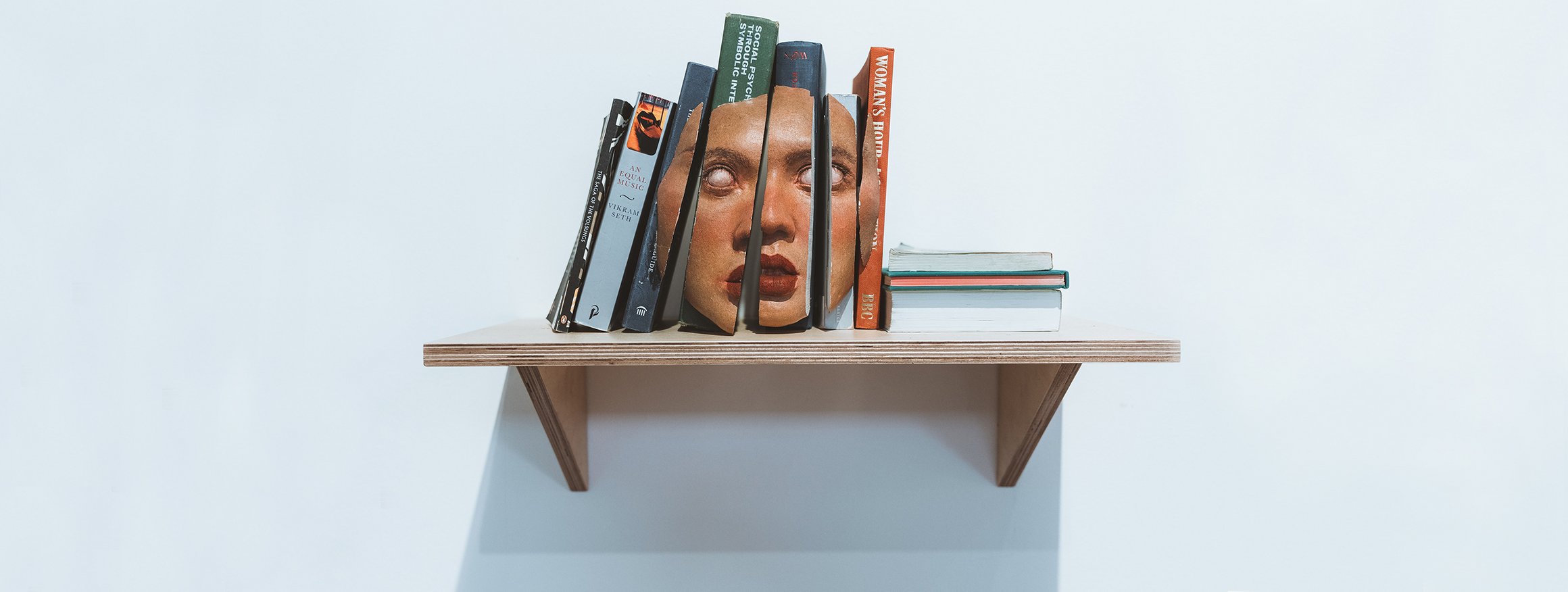 Das Foto zeigt mehrere Bücher, die auf einem Regalbrett stehen. Die Buchrücken ergeben zusammen eine Maske mit ausdruckslosem Blick.