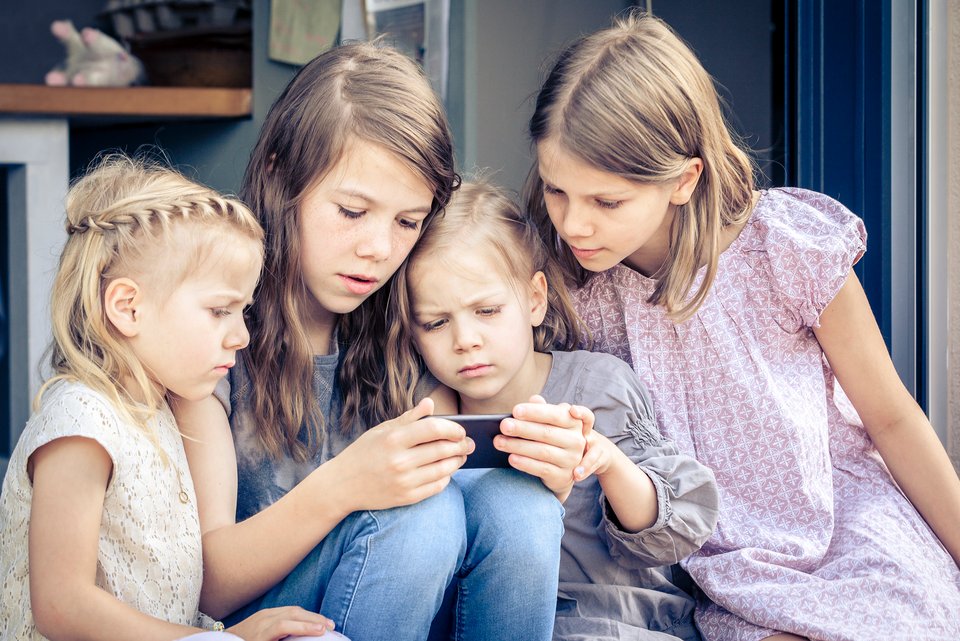 Eine Gruppe junger Mädchen sitzt eng beieinander. Eine von ihnen hält ein Smartphone in der Hand. Die anderen blicken gebannt auf den Bildschirm.