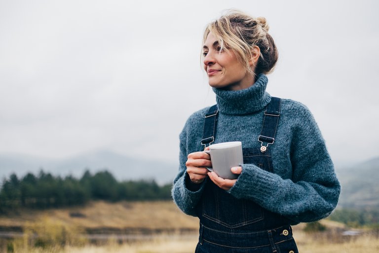 Das Foto zeigt eine Frau mit Pulli und einer Teetasse in der Hand