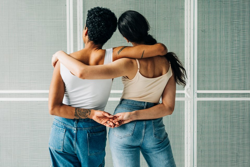 Zwei Frauen von hinten in einer Umarmung und an den Händen haltend 