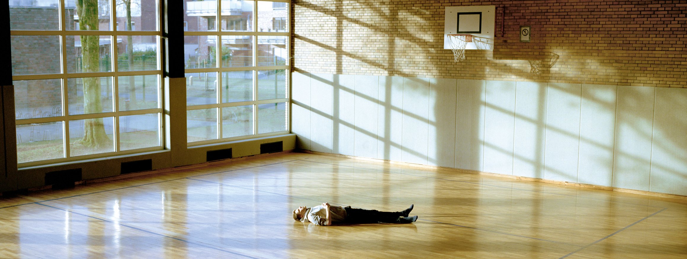 Ein junger Mann liegt in einer Sporthalle traurig auf dem Boden und blickt an die Decke.