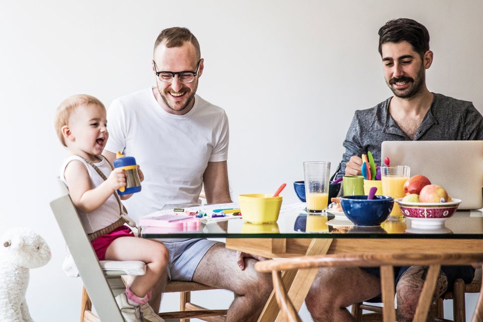 Ein gleichgeschlechtliches Männerpaar sitzt am Tisch mit ihrem fröhlichen Kind