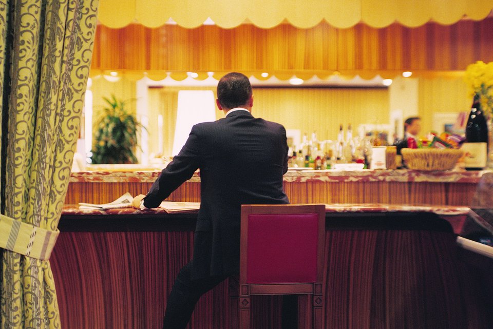 Ein Mann im Anzug sitzt auf einem Barhocker am Tresen einer Bar