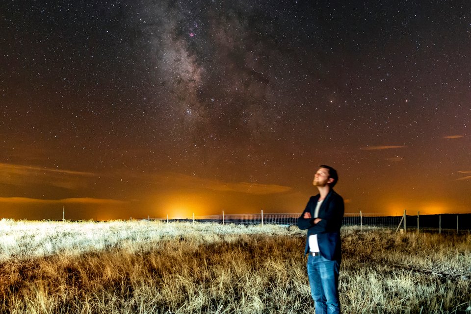 Ein Mann steht auf einer Wiese und schaut interessiert in den Nachthimmel, der voller Sterne ist