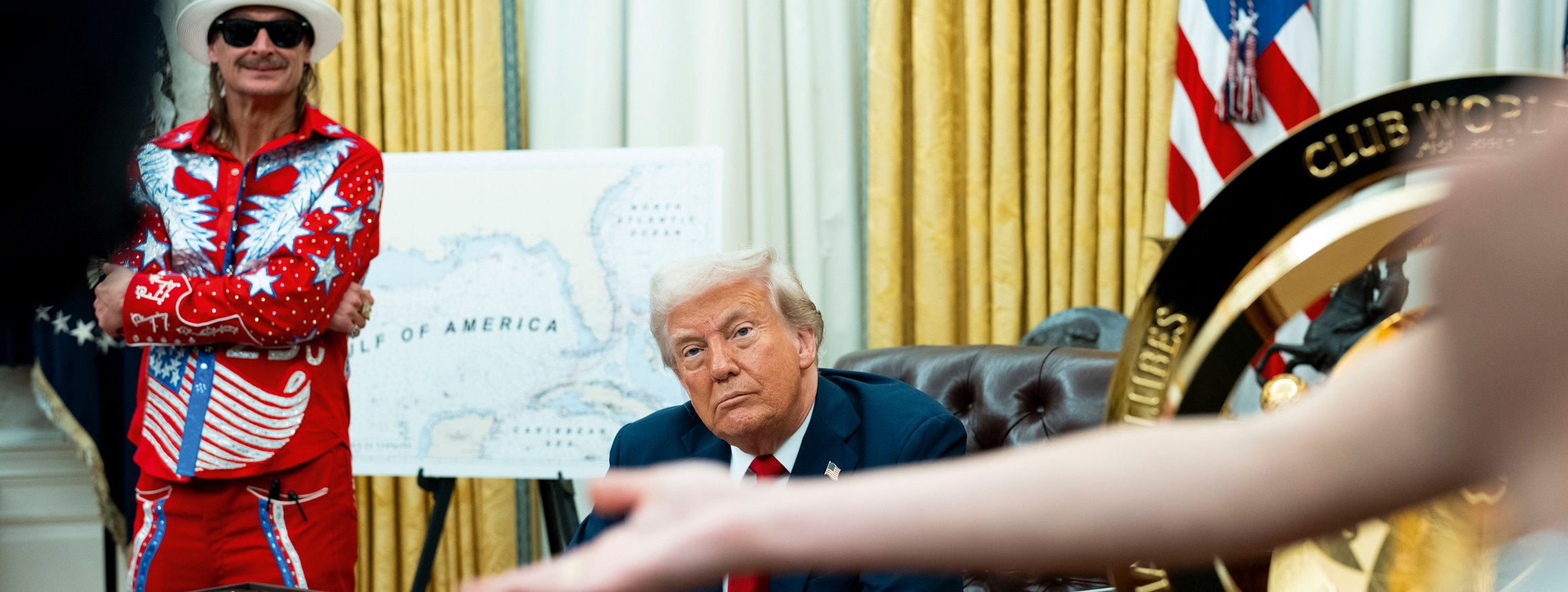 Der US-Präsident Donald Trump sitzt an seinem Schreibtisch an einem Regierungsdekret, das er unterzeichnet hat, während neben ihm der Musiker Kid Rock in einem bunten Cowboykostüm steht