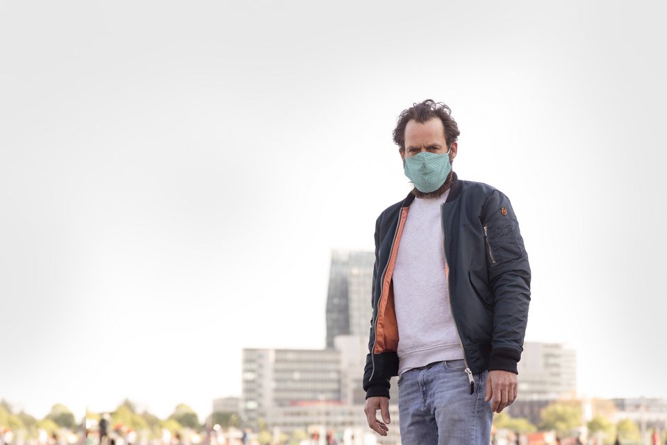 Foto zeigt einen Mann mit Coronaschutzmaske vor der Skyline einer Stadt.