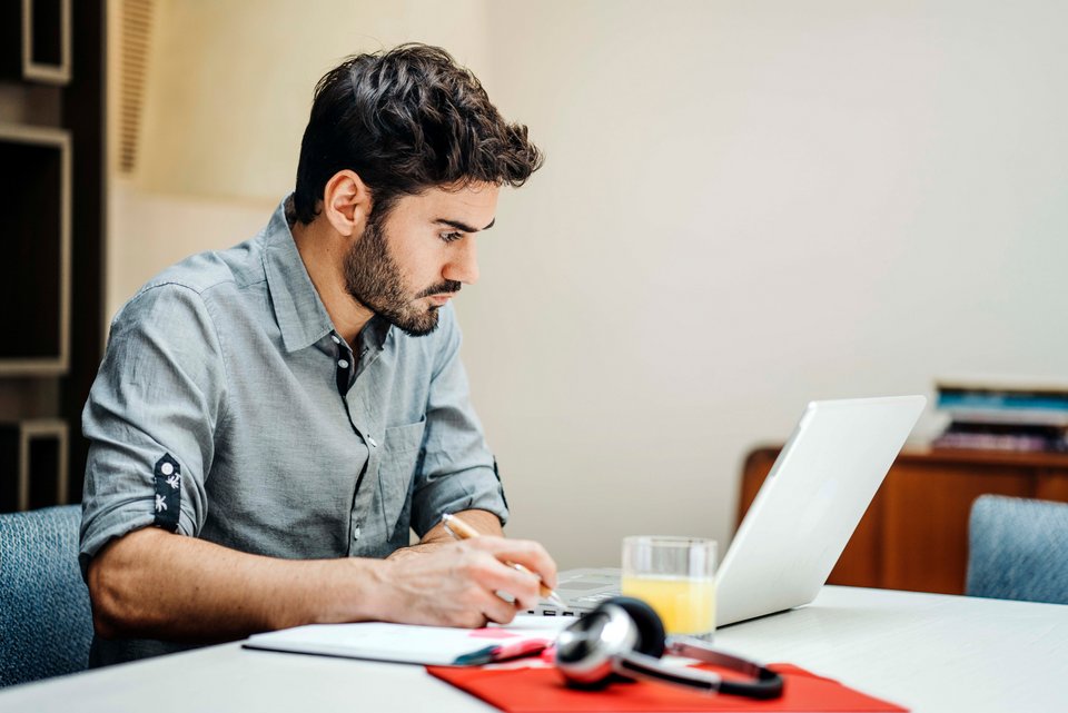Ein junger Mann mit dunklem Bart sitzt an seinem Schreibtisch und verfolgt auf dem PC-Bildschirm seinen Online-Studiengang