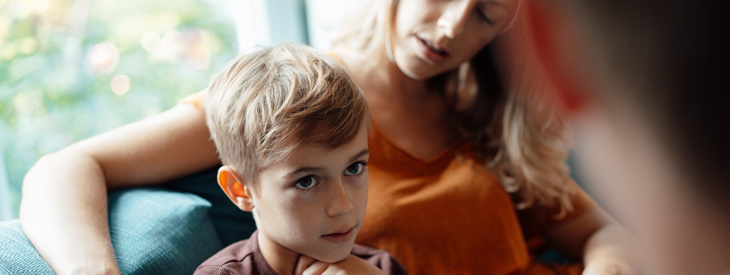 Ein Junge sitzt bei seiner Mutter, die ihren Arm um das Kind gelegt hat, und der seinem Vater anschaut, der vor ihm sitzt 