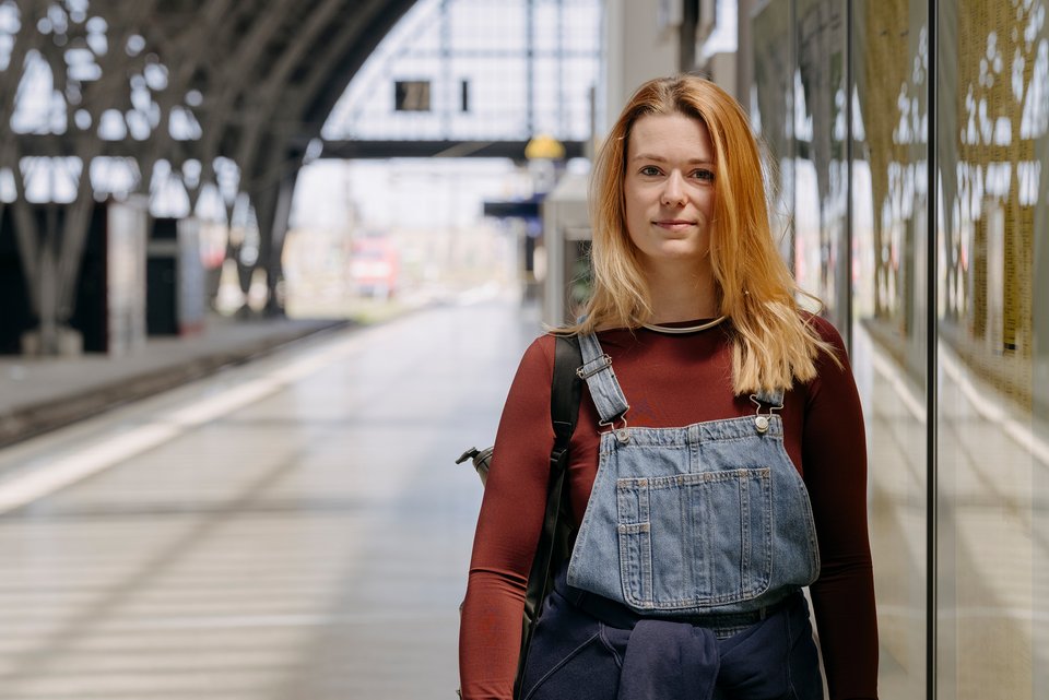Christina Fetzer, die sich bei der European Dyslexia Association engagiert, steht mit Rucksack an einem Bahnhof und schaut entspannt, da sie keine Angst mehr vor Dyskalkulie hat