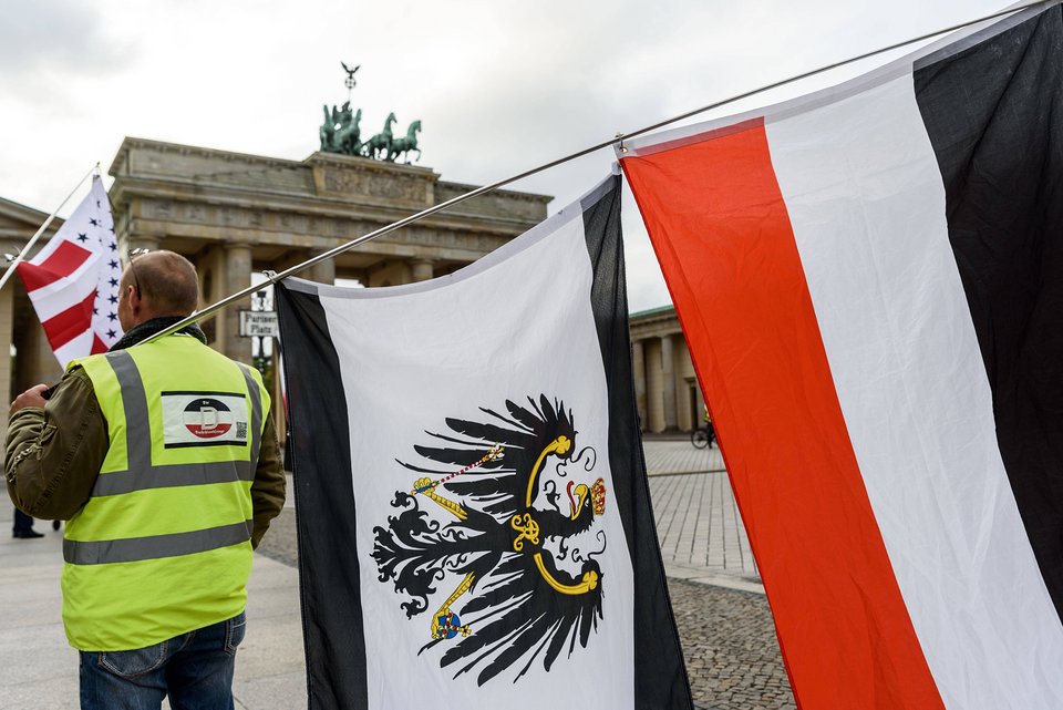 Ein Reichsbürger trägt auf einer Demonstration am Brandenburger Tor eine gelbe Weste mit Deutschland-Symbol und zwei Flaggen