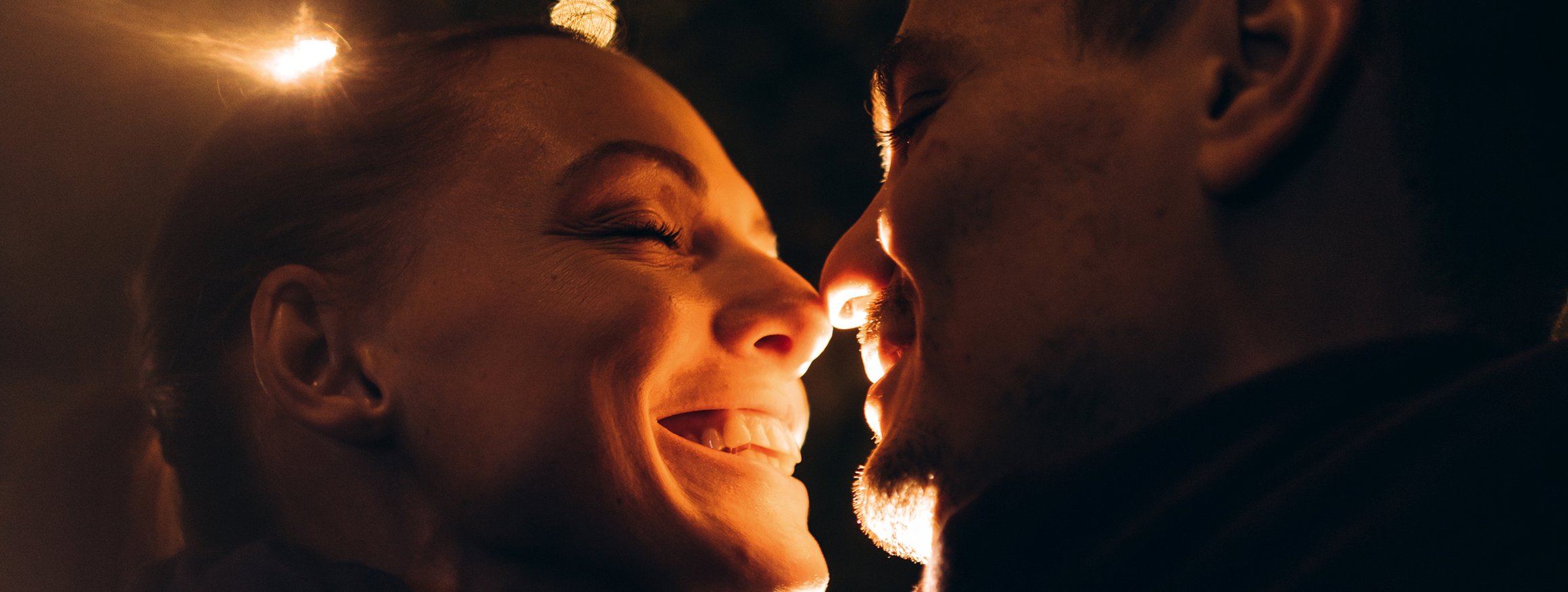 Ein Paar steht verliebt lächelnd beieinander mit geschlossenen Augen und die Nasenspitzen berühren sich