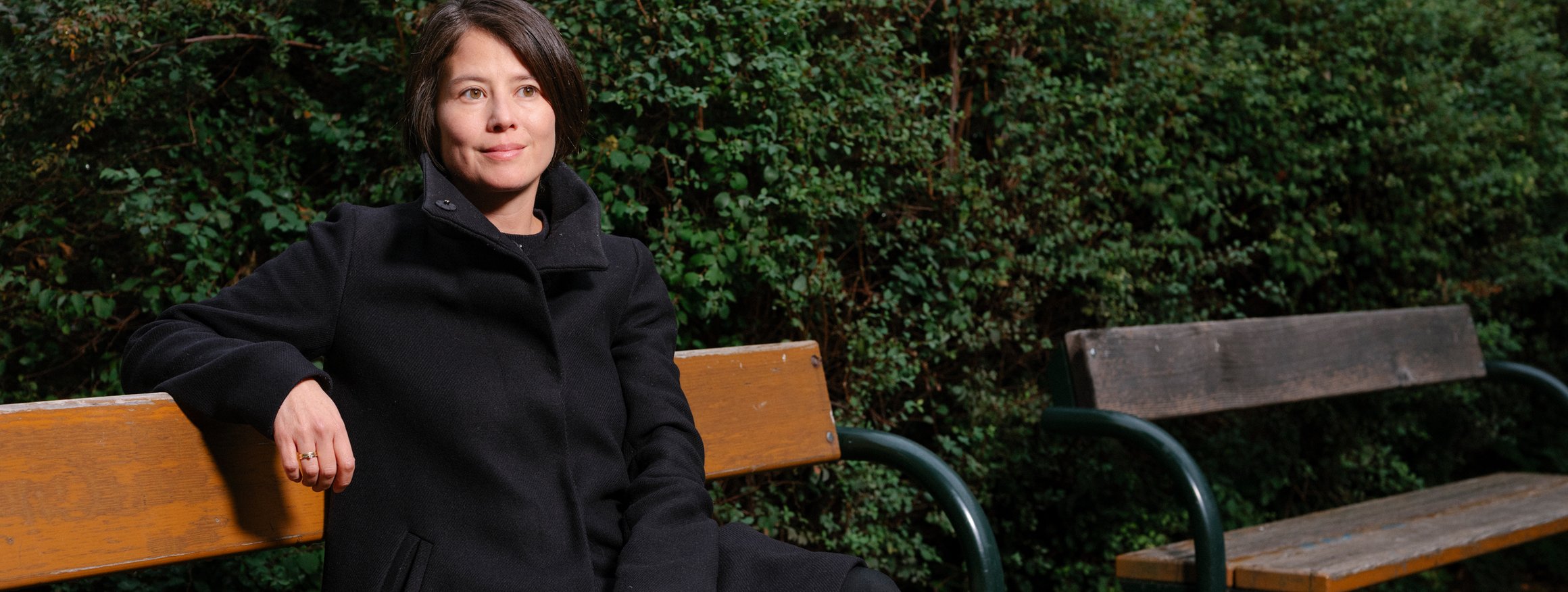 Die Autorin Milena Michiko sitzt auf einer Parkbank vor einer grünen Hecke.