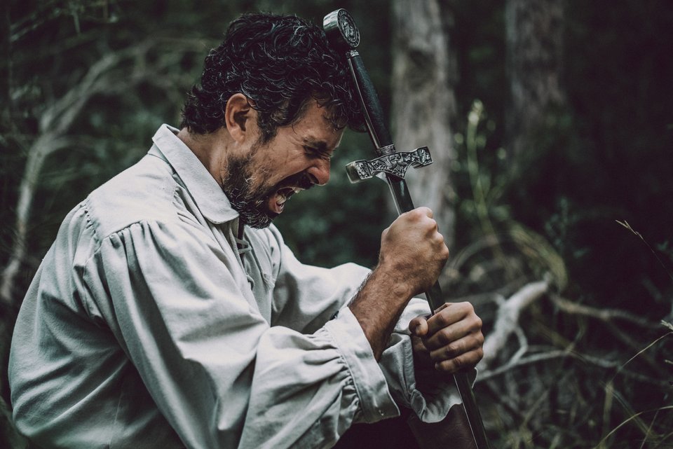Ein Schauspieler mit einem altertümlichen Hemd umfasst verzweifelt ein Schwert, wobei er seinen Emotionen freien Lauf lässt und in seiner Rolle aufgeht