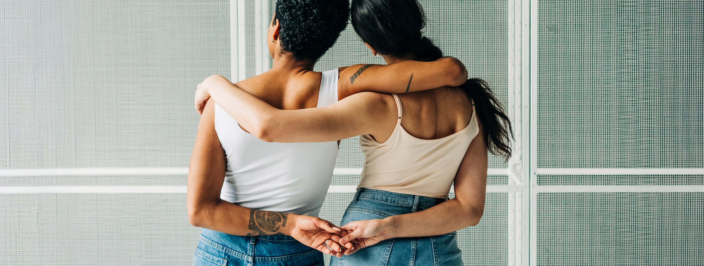 Zwei Frauen von hinten in einer Umarmung und an den Händen haltend 