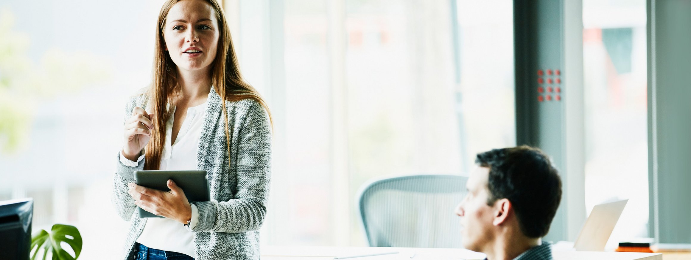 Eine junge Frau steht selbstbewusst im Konferenzzimmer und redet, während ihr ein Kollege zuhört