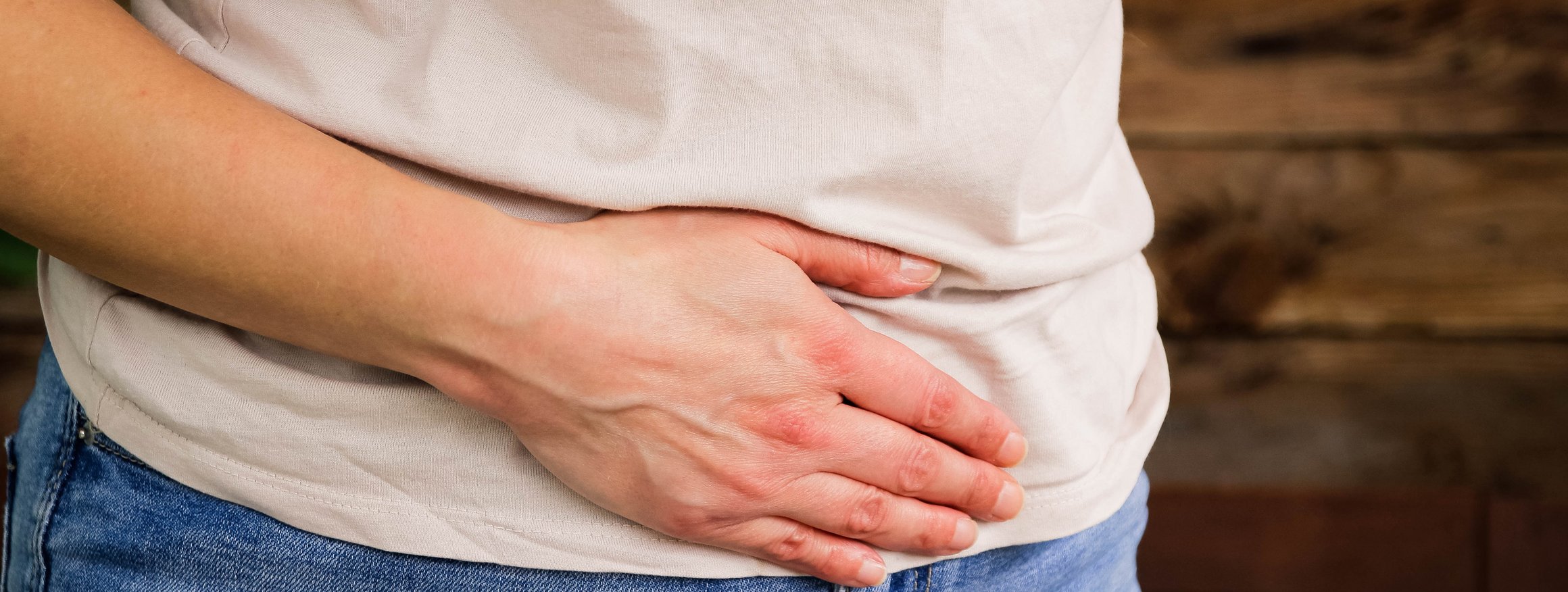 Eine Frau in Jeans und weißem T-Shirt hält sich mit der Hand den Bauch