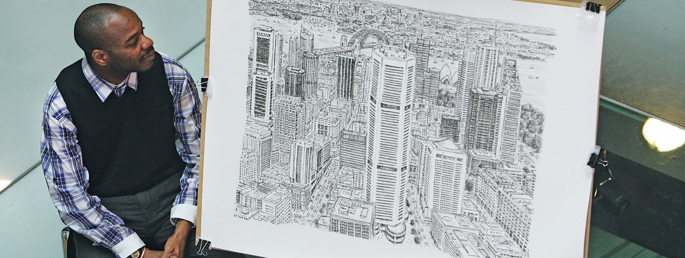 Der britische Künstler Stephen Wiltshire hat eine Autismus-Spektrum-Störung und sitzt vor seinem gezeichneten Bild, das eine große Stadtkulisse zeigt, die er exakt aus dem  Gedächtnis gezeichnet hat