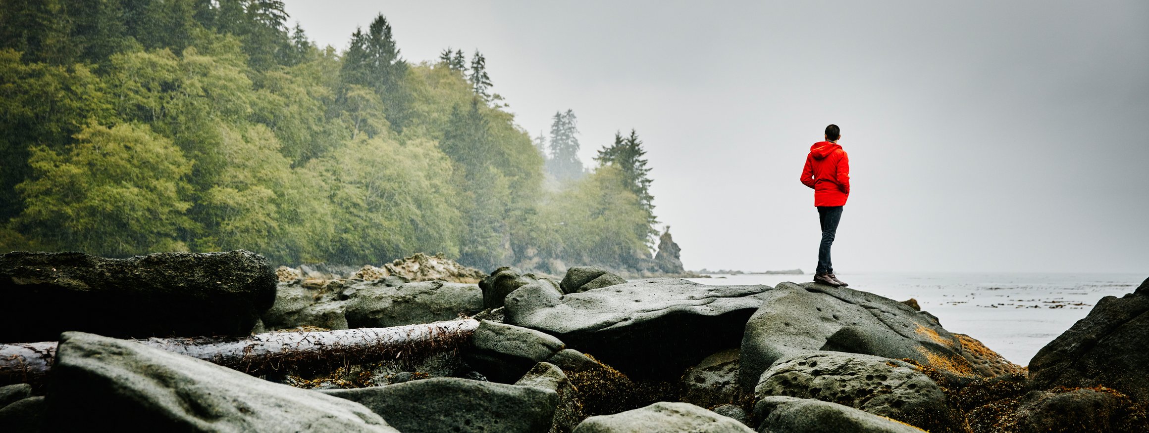 Ein Mann im roten Anorak steht allein auf einem Felsen am Meer