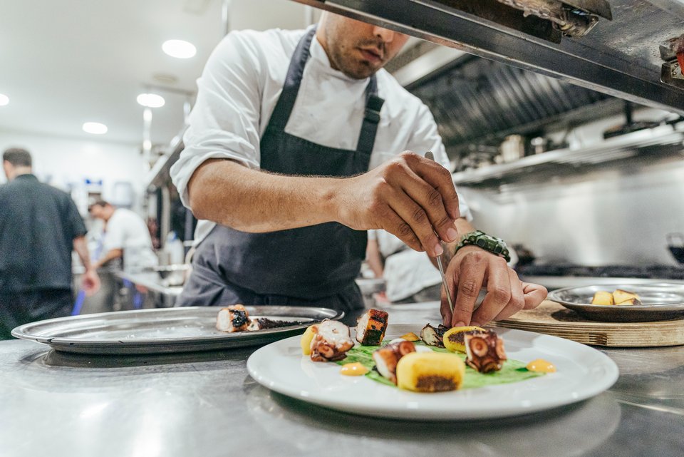 Ein Koch steht in einer Restaurantküche und bereitet einen Teller zu