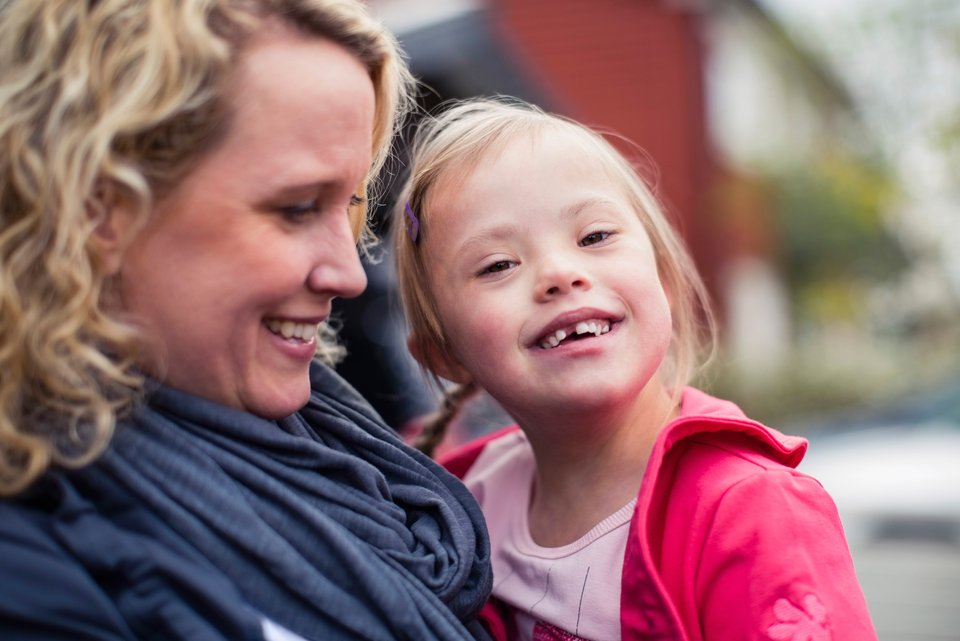 Eine Mutter hält lächelnd ihr fröhliches Kind im Arm, dass das Downsyndrom hat