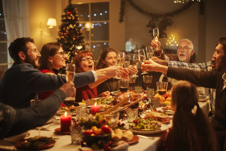 Eine Familie sitzt an Weihnachten am festlich gedeckten Tisch und prostet sich zu.