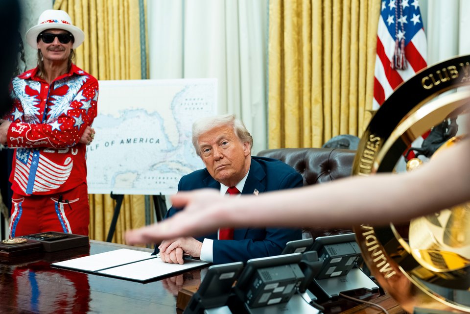 Der US-Präsident Donald Trump sitzt an seinem Schreibtisch an einem Regierungsdekret, das er unterzeichnet hat, während neben ihm der Musiker Kid Rock in einem bunten Cowboykostüm steht