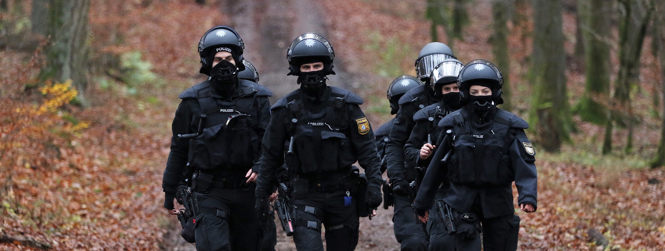 Eine Gruppe von Polizistinnen und Polizisten mit Helmen und schwarzer Einsatzkleidung laufen auf einem Waldweg in Richtung Dannenröder Forst