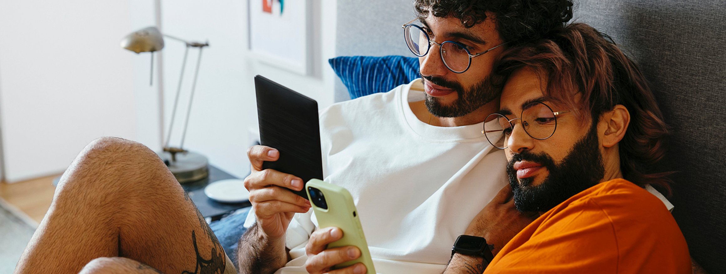 Ein Paar liegt eng beieinander, während jeweils beide ein Smartphone in der Hand halten und darauf schauen