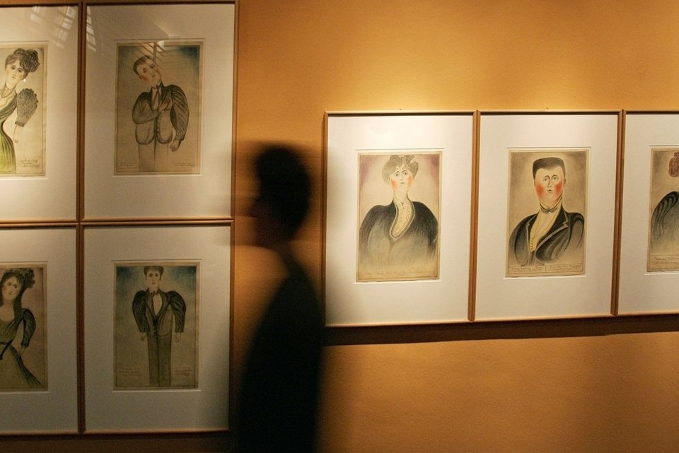 Das Foto zeigt eine menschliche Silhouette, die an Gemälden vorbeiläuft. Die Kunstwerke zeigen Selbstporträts von Psychiatrie-Erfahrenen.