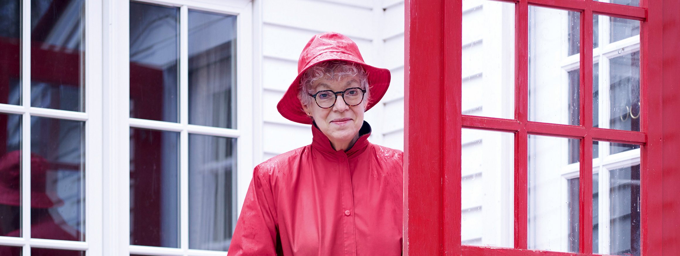 Die renommierte Psychologin und Princeton-Professorin Susan Fiske, steht im roten Regenmantel und rotem Hut an ihrer roten Eingangstür