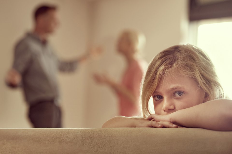 Ein kleines blondes Mädchen schaut traurig, weil ihre Eltern im Hintergrund streiten